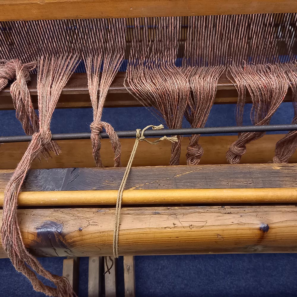 A colourful selection of woolen spools on the floor beside a loom.