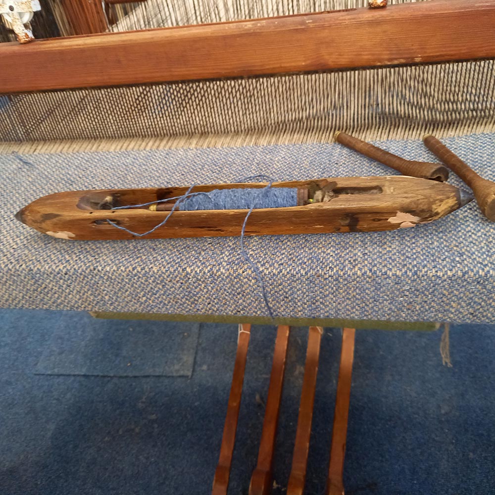 A colourful selection of woolen spools on the floor beside a loom.